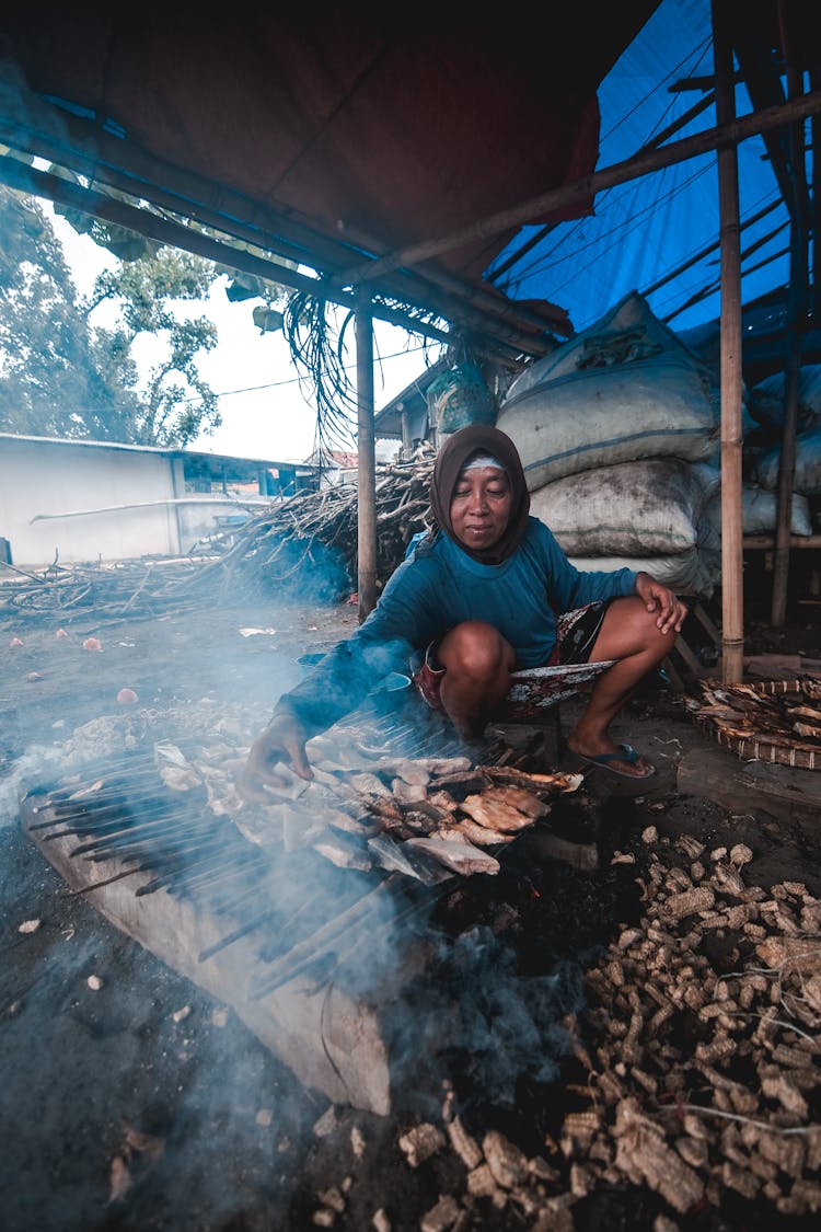 Woman Grilling Fish Under A Roof 