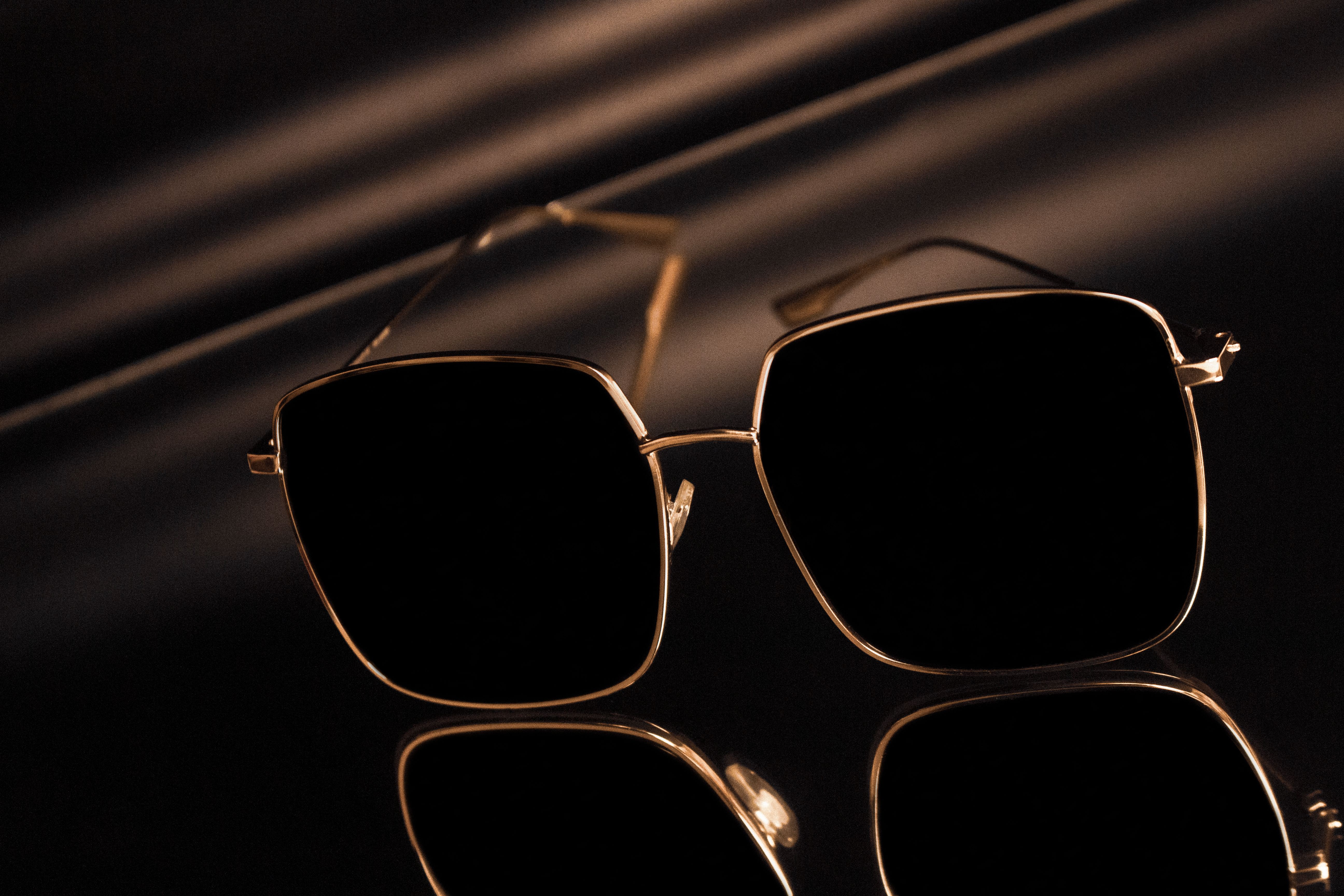 Stylish square sunglasses with gold frames reflecting on a glossy surface.