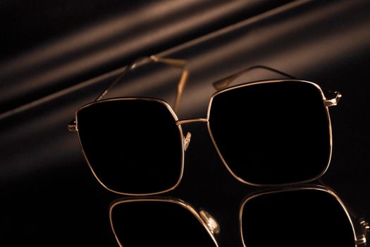Stylish square sunglasses with gold frames reflecting on a glossy surface.