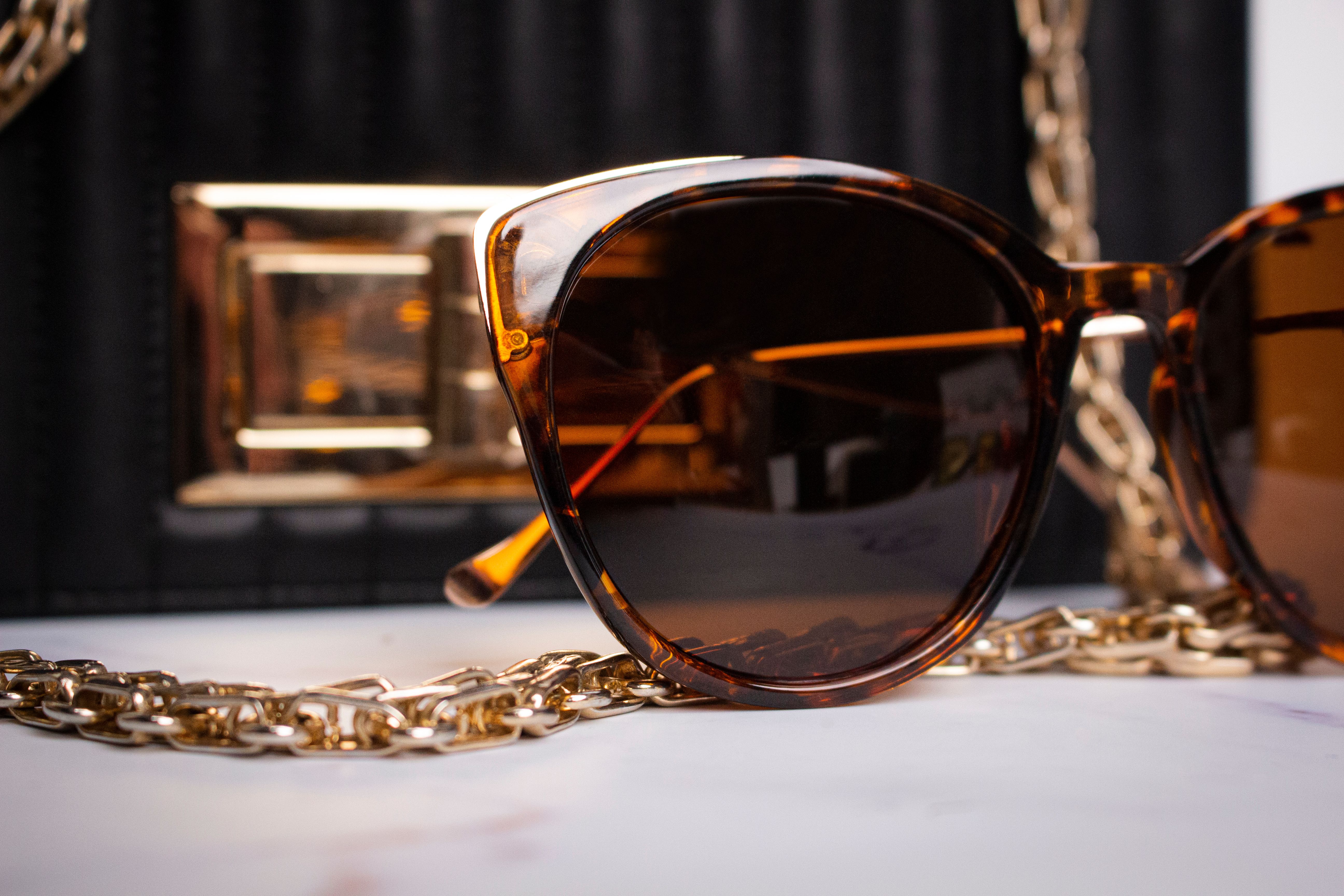 Close-up of stylish tortoise shell sunglasses paired with a luxurious gold chain and classic black handbag.