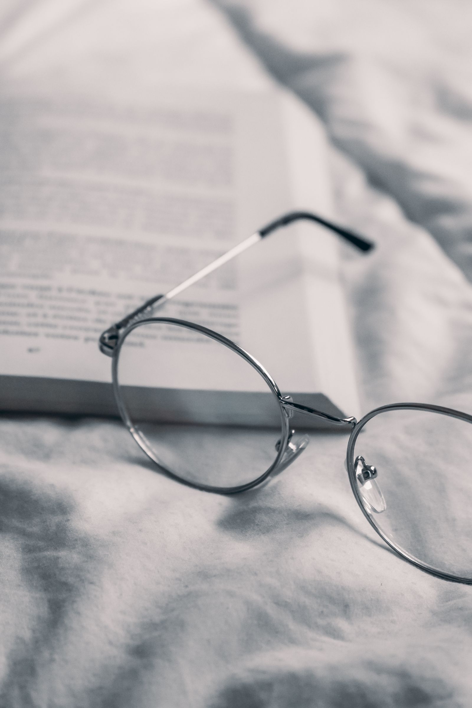 Round wire glasses resting on an open book on grey bedding