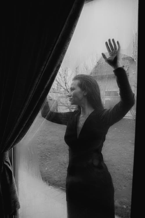 A Grayscale of a Woman Leaning on a Glass Window