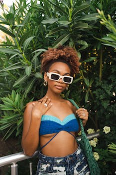 Stylish woman with sunglasses in bikini top and shorts posing by lush greenery, capturing a summer vibe.