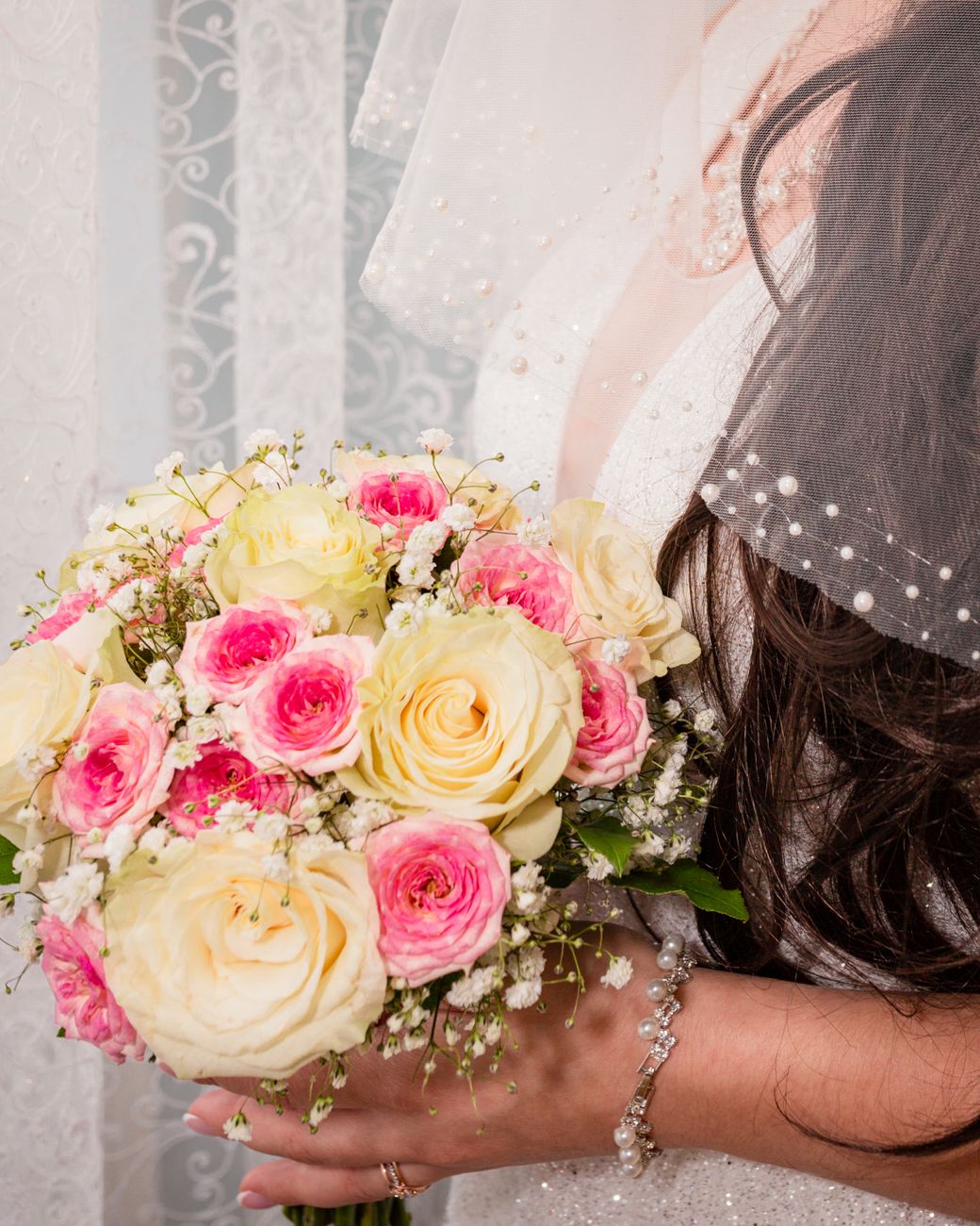 Close-up of a bride holding a beautiful bridal bouquet with roses and greenery.