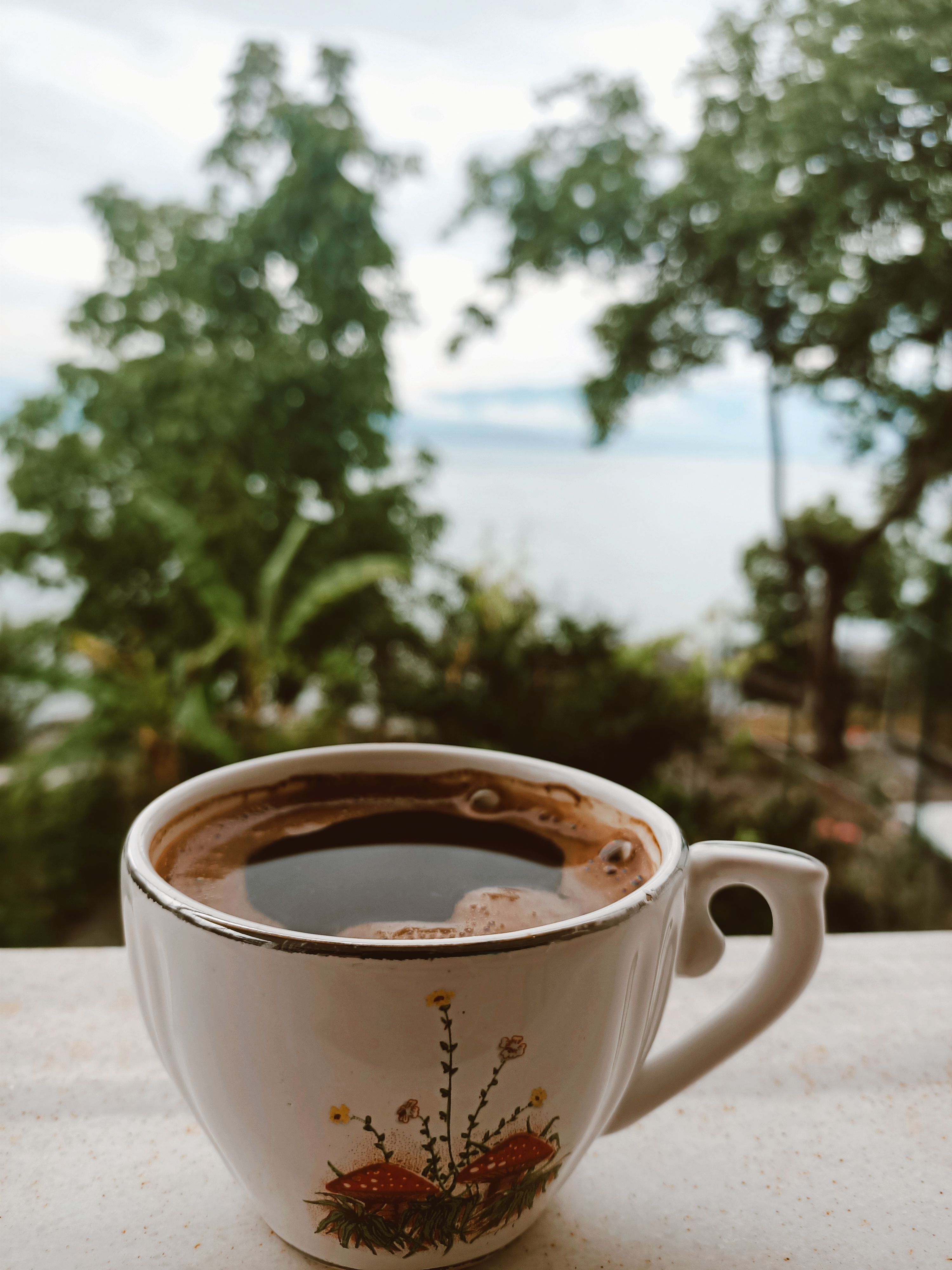 Free A detailed close-up of a coffee cup with a peaceful outdoor view, perfect for morning vibes. Stock Photo