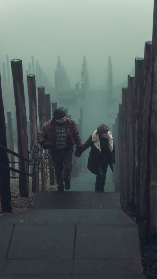 An Elderly Couple Holding Hands While Walking up a Foggy Stairway