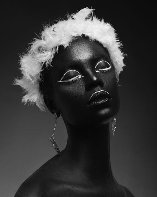 Captivating black and white portrait of a woman with striking feathered accessories and artistic makeup.
