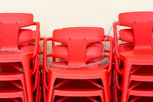 Free A stack of red plastic chairs secured with chains against a neutral background. Stock Photo