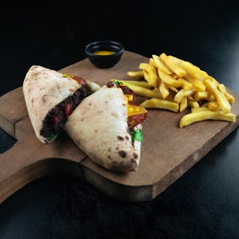A mouthwatering pita sandwich with fresh ingredients alongside crispy french fries on a stylish wooden board.