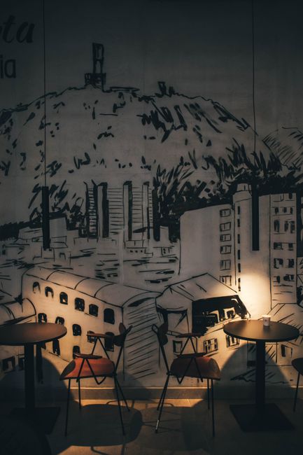 Cozy coffee shop setting with artistic wall mural, tables, and warm lighting ambiance.