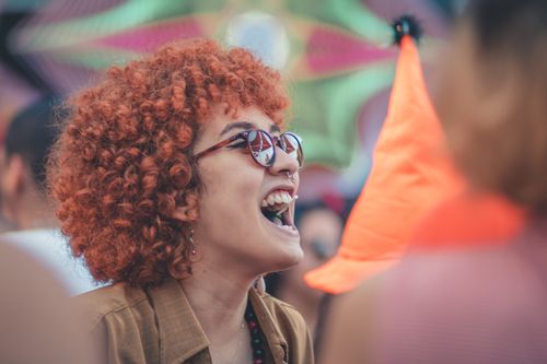 Free A vibrant scene of a smiling woman with curly hair enjoying an outdoor festival, exuding joy and liveliness. Stock Photo