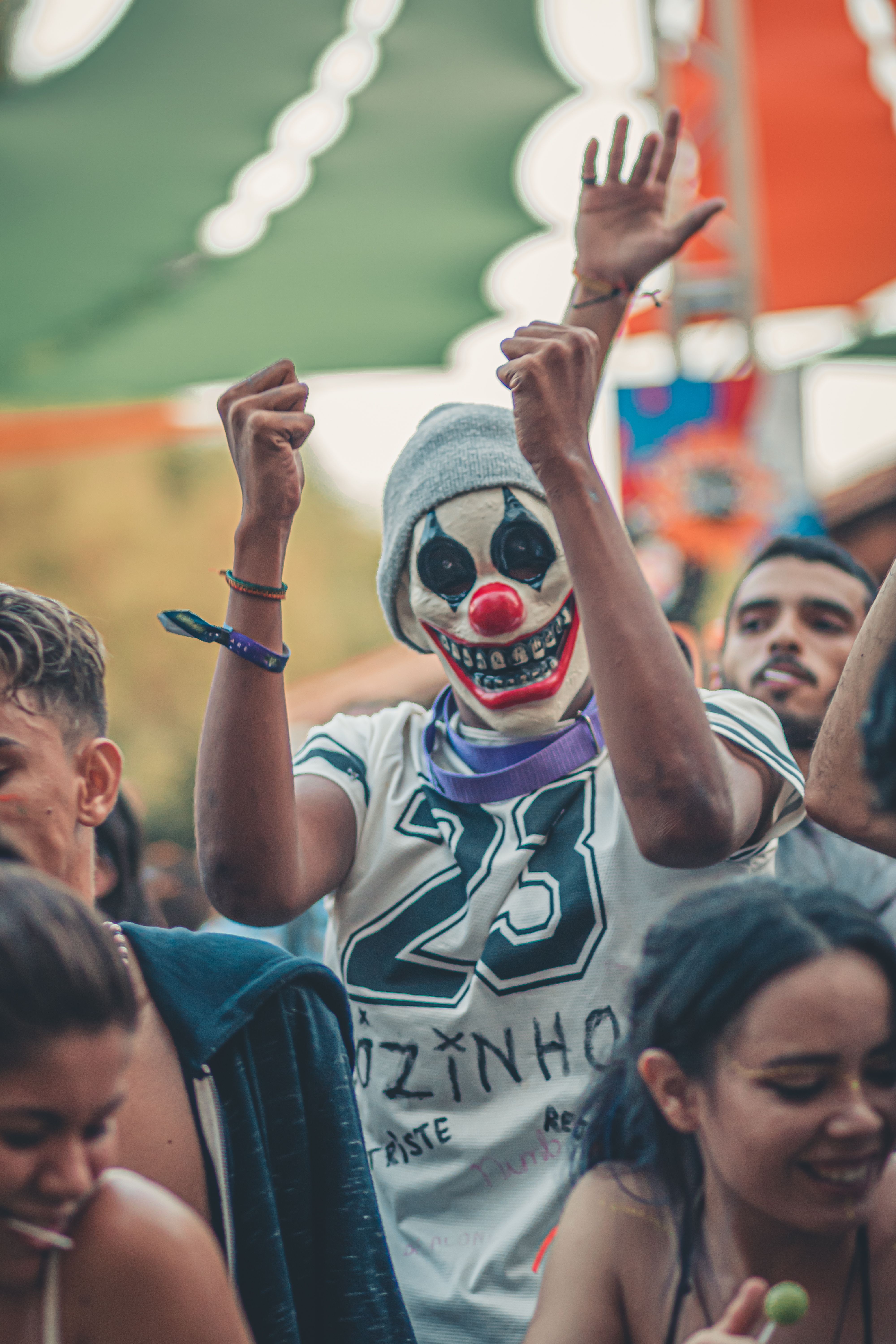 Energetic crowd enjoying an outdoor concert with a masked participant raising hands in excitement.