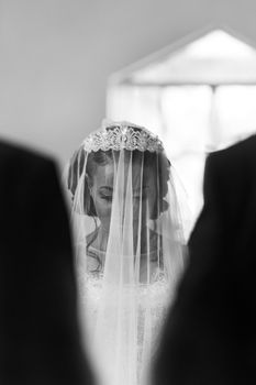A beautiful black and white portrait of a bride with a veil during a wedding ceremony.