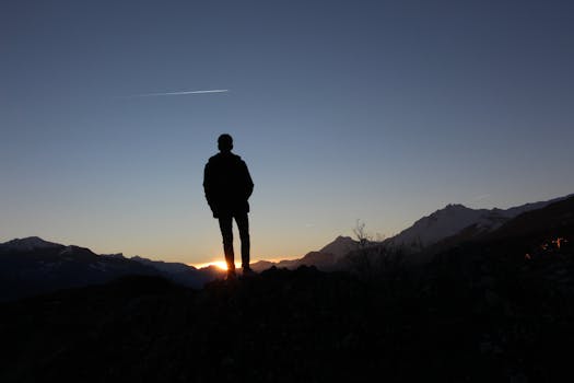 Person silhouette on mountain during sunset, capturing peaceful moment.