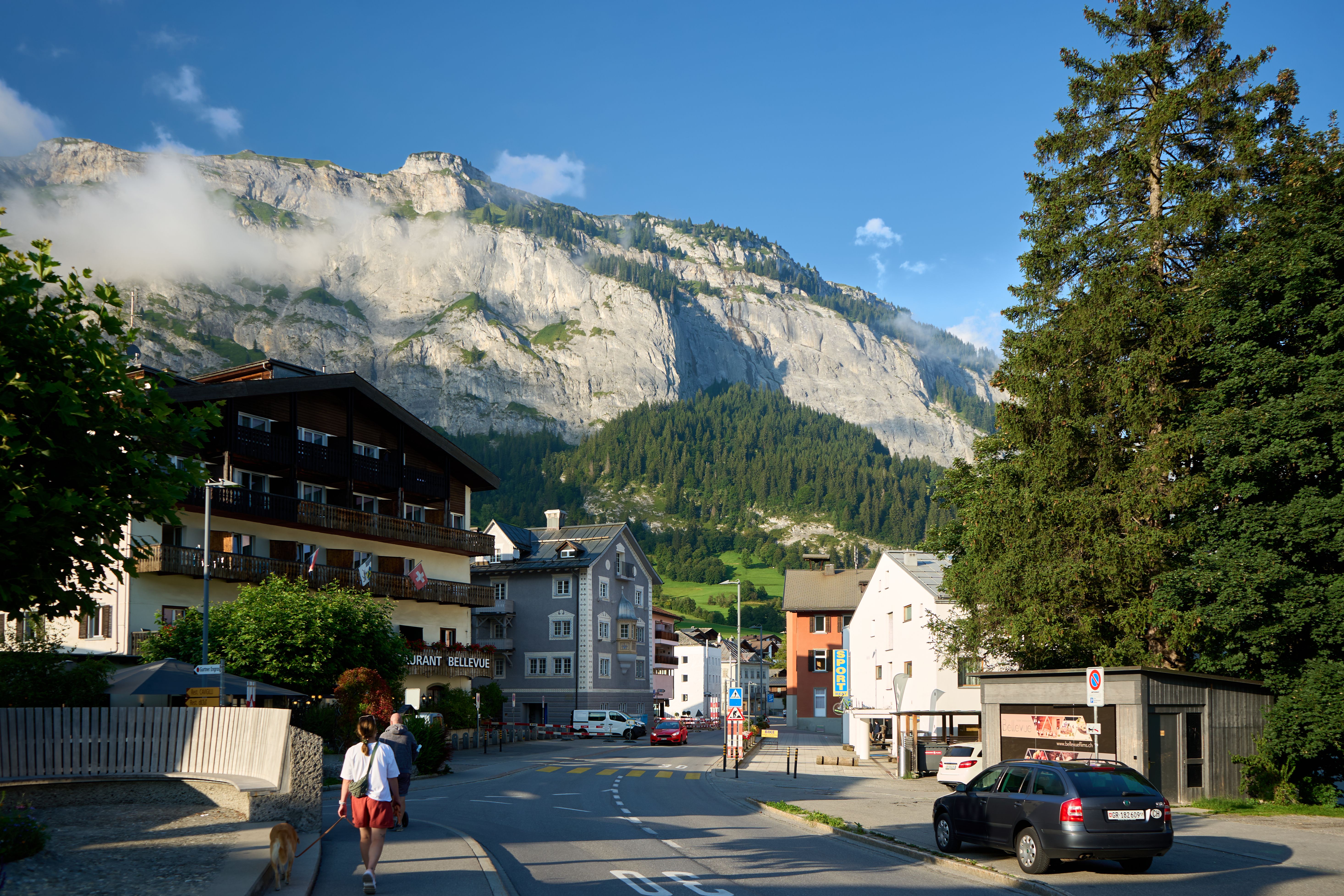 Scenic view of a mountain village with people walking under a clear blue sky.