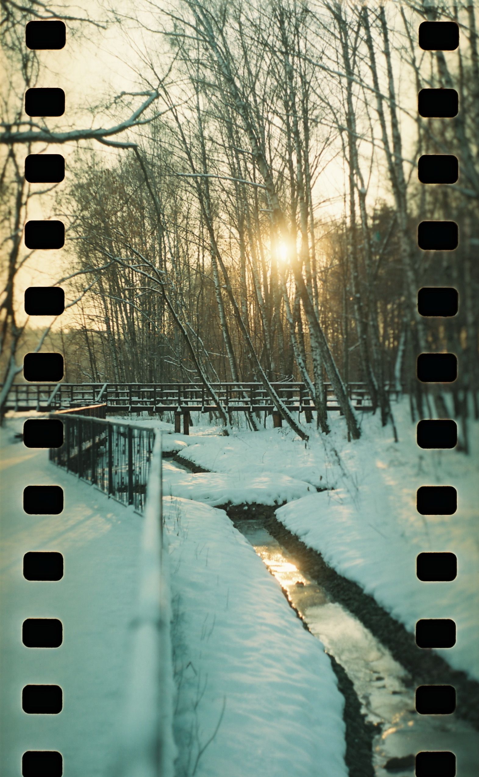 A tranquil winter landscape in a snowy forest with a stream, captured at sunset.