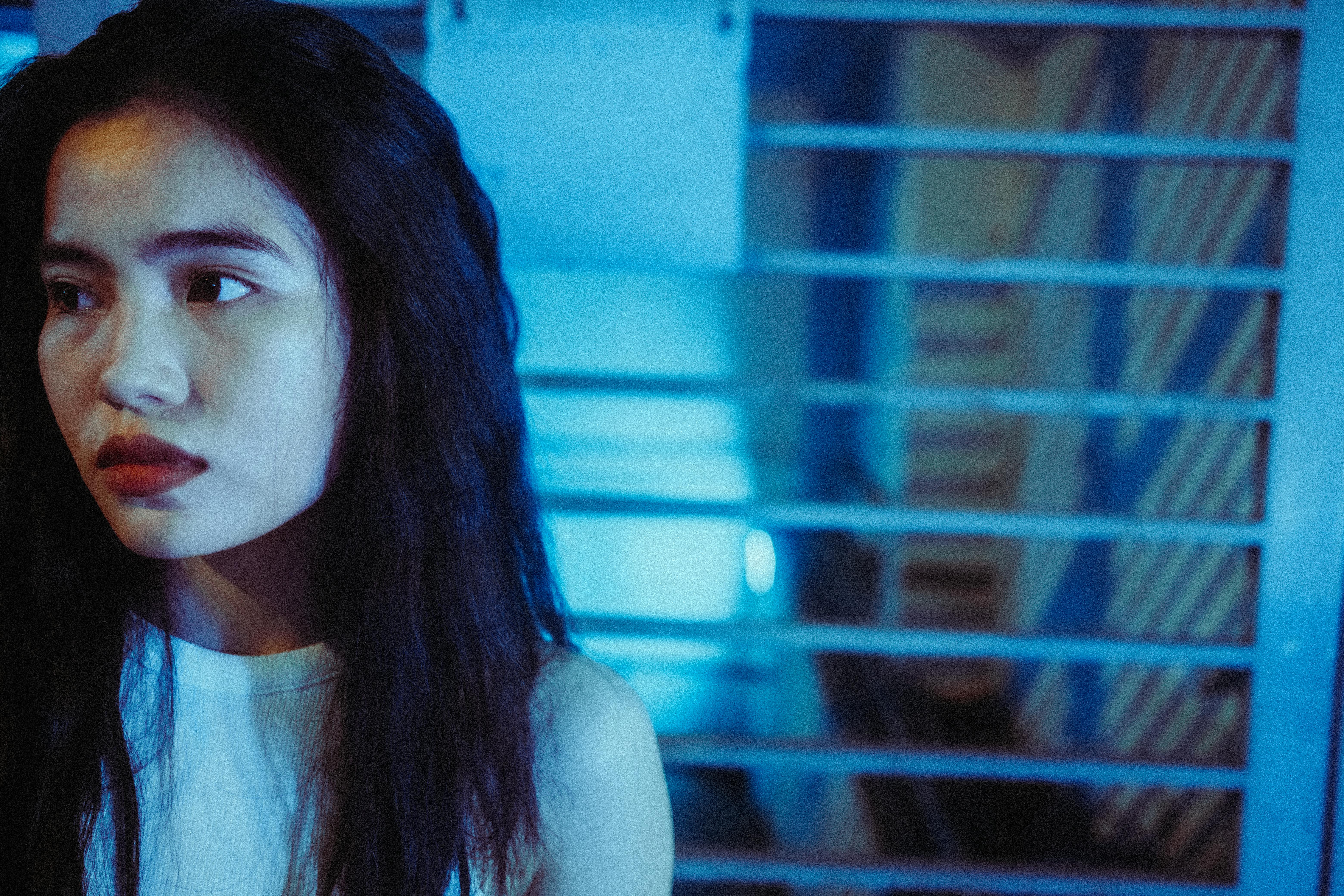 Close-up portrait of an Asian woman in a blue-toned setting with a moody atmosphere.