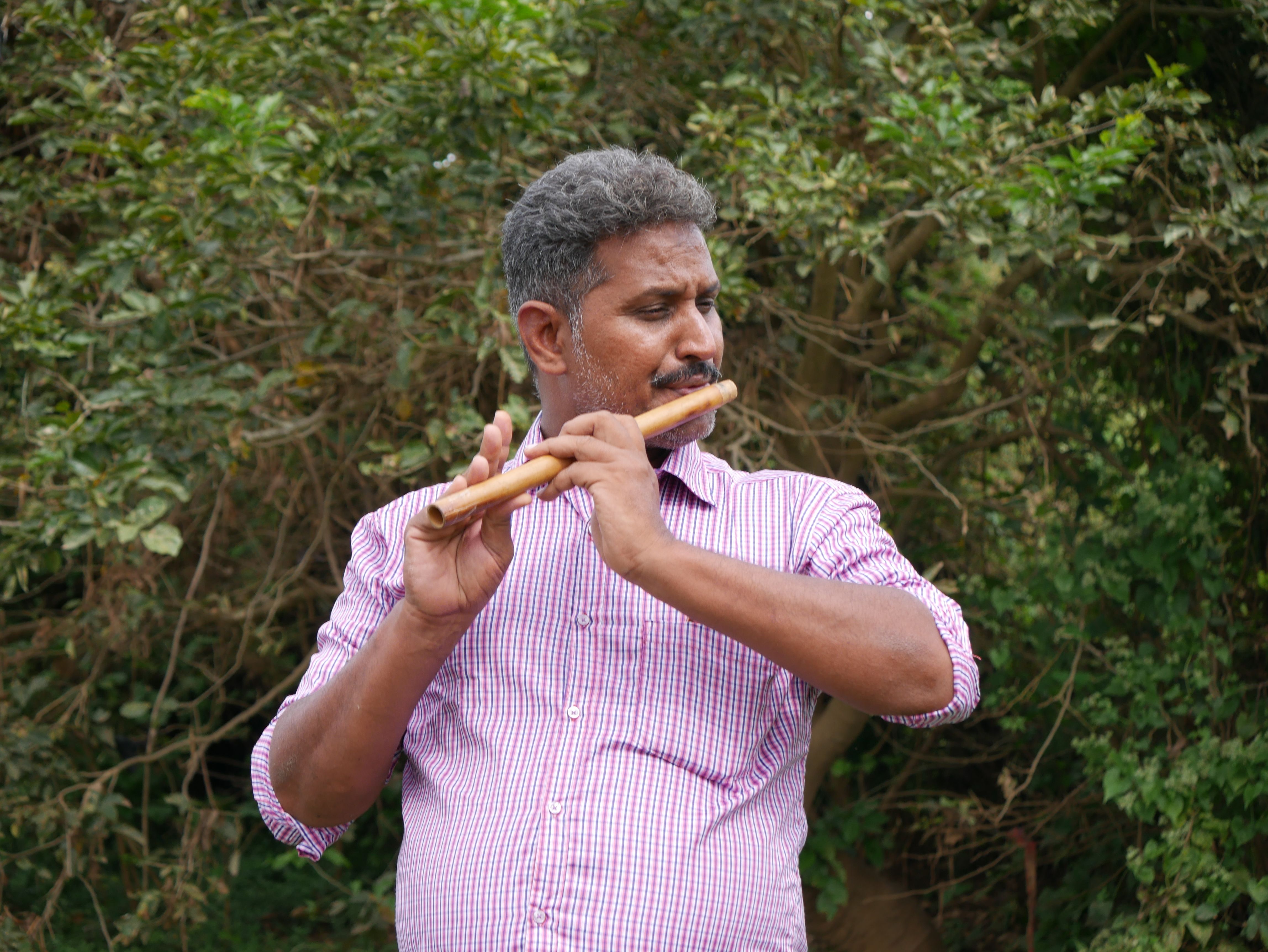 Elderly man playing the flute in a serene outdoor setting with lush green background.