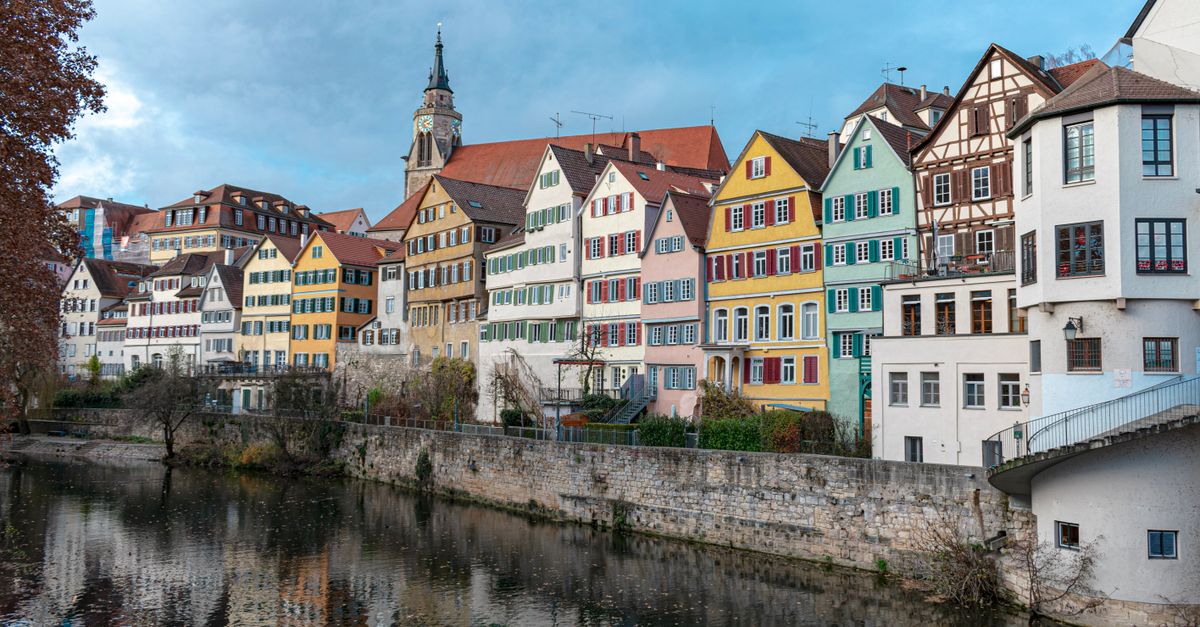 colorful medieval houses reflected in a calm river, Alps in background