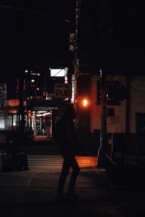 Free A person walks past a dimly lit pub on a city street at night, creating a dramatic silhouette. Stock Photo