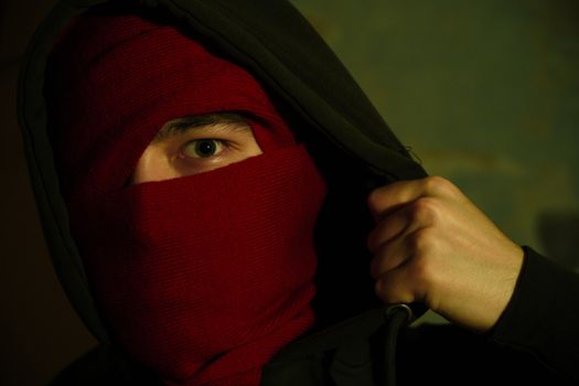 Close-up of a person with a red scarf and hood, focusing on the eye, creating a sense of mystery.