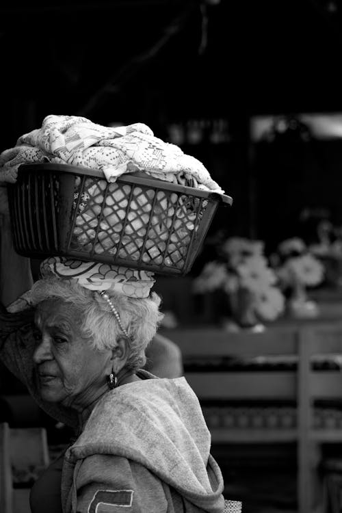 Free Grayscale Photo of an Elderly Woman Holding a Basket on Her Head Stock Photo