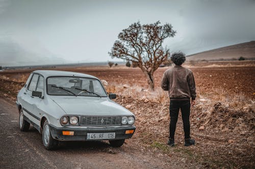 Man in Brown Jacket Standing Beside Gray Vintage Car