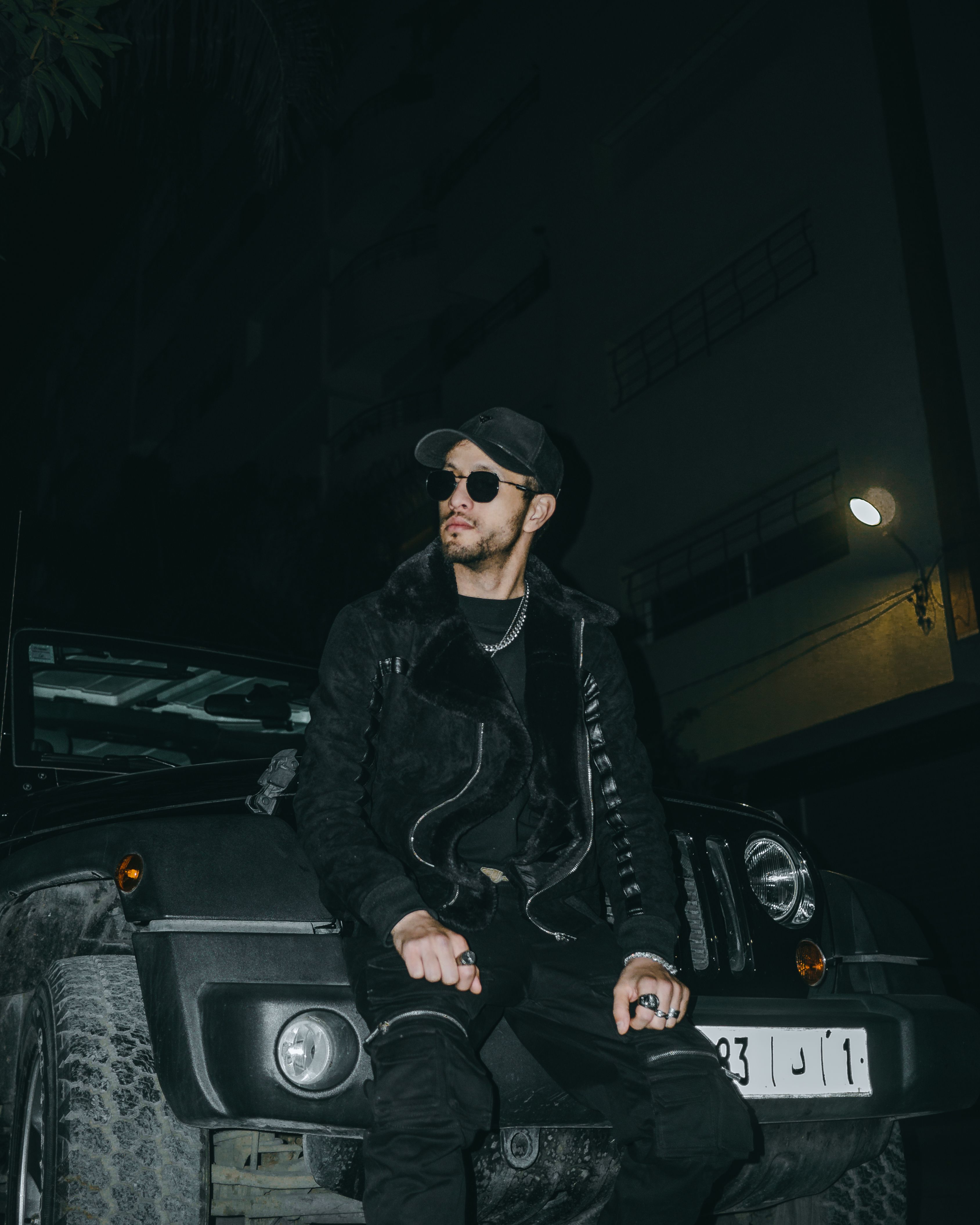 A fashionable man poses by a Jeep at night in Fes, Morocco, showcasing urban style.
