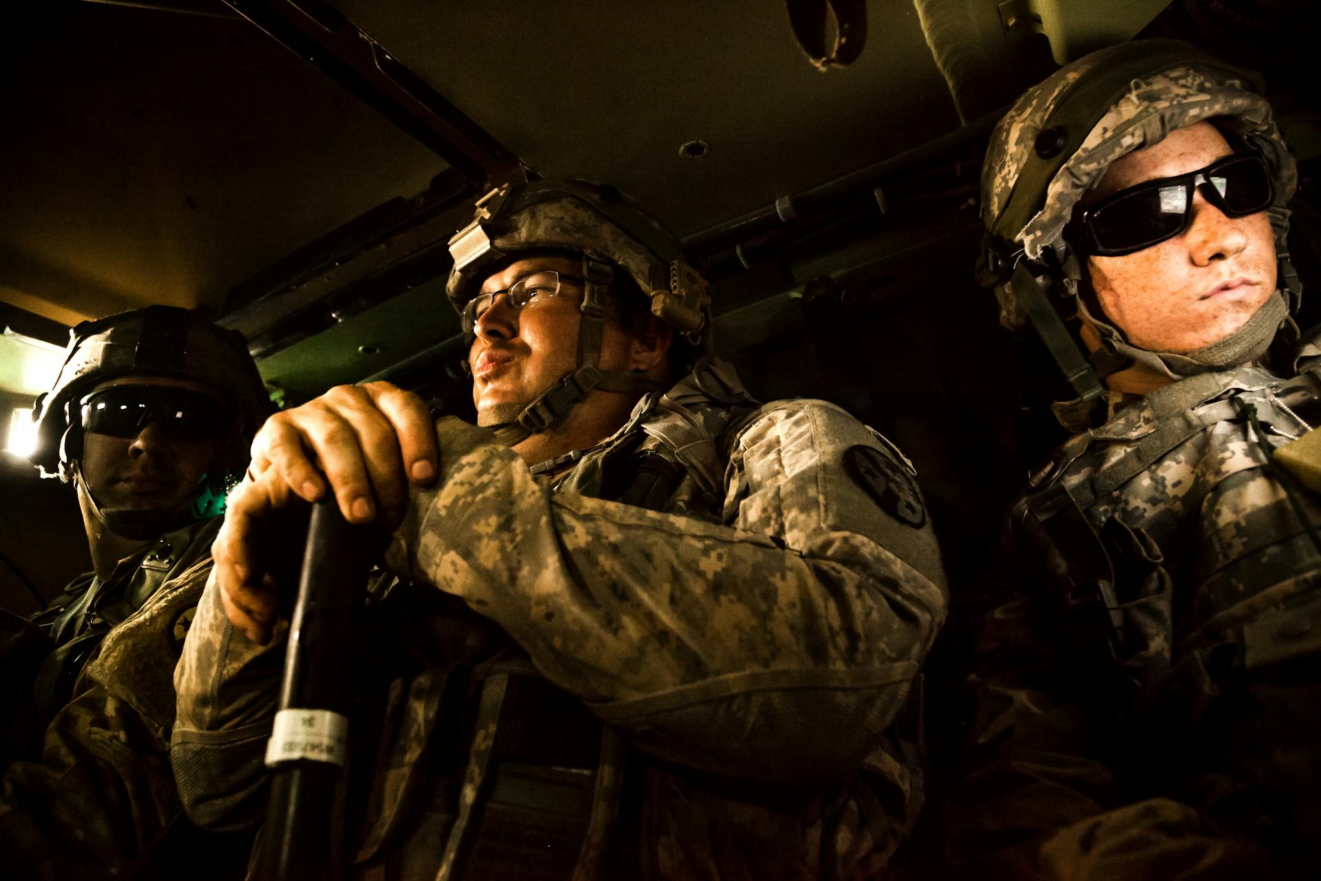 Three soldiers in military uniform inside an armored vehicle, prepared for action.