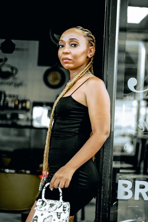 Free Elegant African woman in a black dress posing indoors with a stylish handbag. Trendy and fashionable look. Stock Photo