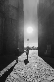 Black and white photo capturing silhouettes against sunlight in a historic Porto courtyard.