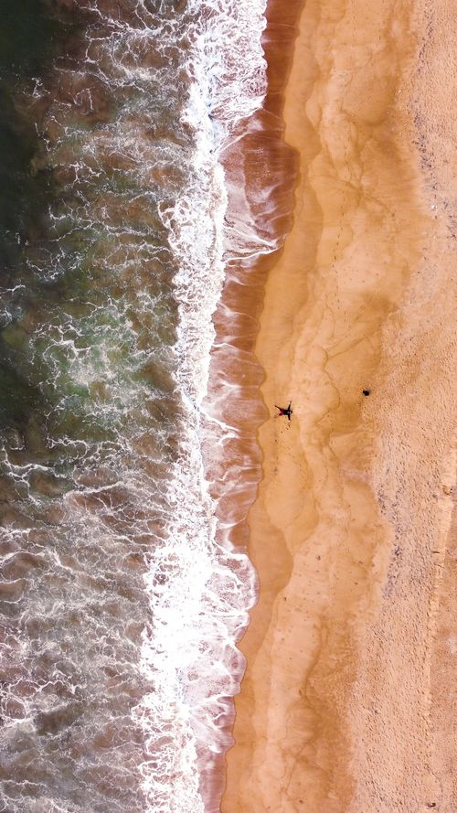 Free Stunning aerial view of a sandy coastline with waves crashing onto the shore, captured from above. Stock Photo