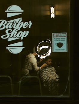 Barber shop interior with client and barber, seen through glass wall. Calm and warm atmosphere.