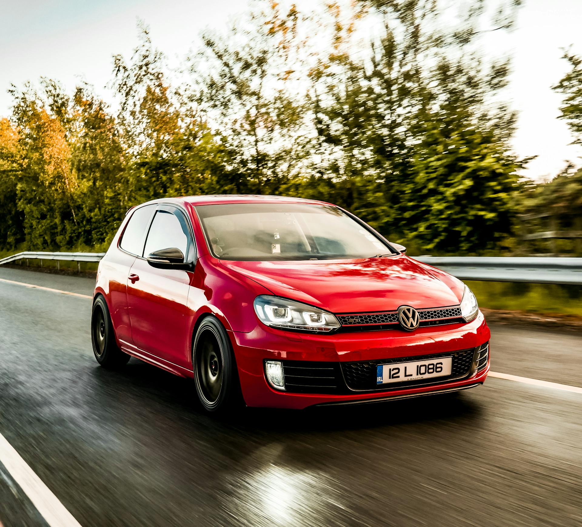 Dynamic shot of a red Volkswagen hatchback driving on a scenic Irish road.