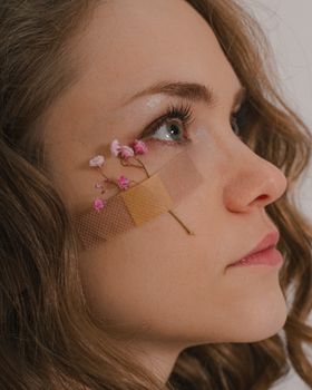 Artistic side view of woman with flowers and band aid on face, showing creativity and beauty.