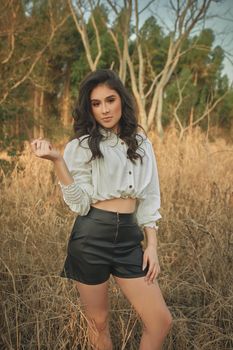 Chic woman in a natural setting posing confidently amidst dry grasses.