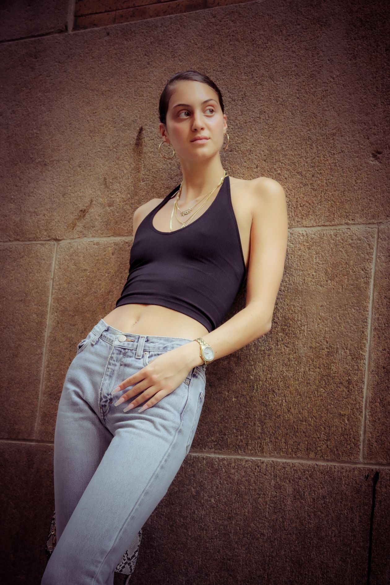Woman in a black halter-neck top and light-wash jeans against a stone wall