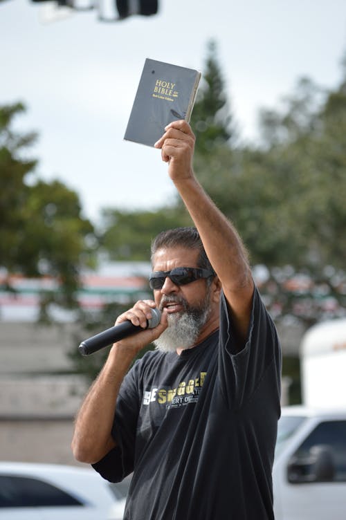 A Man Talking on a Microphone while Holding a Bible