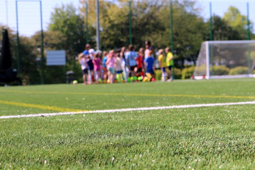 A group of children practicing soccer on a lush green field under a clear blue sky.