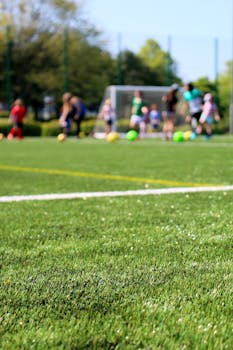 Blurred children playing soccer on a vibrant green field during a sunny day.
