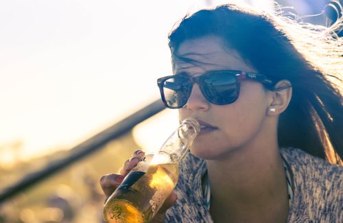 Free Lady savoring a cold beer while enjoying a sunny day outdoors in stylish sunglasses. Stock Photo