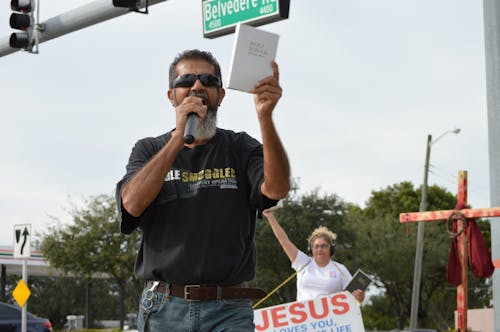 Man in Black Shirt Talking on Microphone While Holding a Bible 