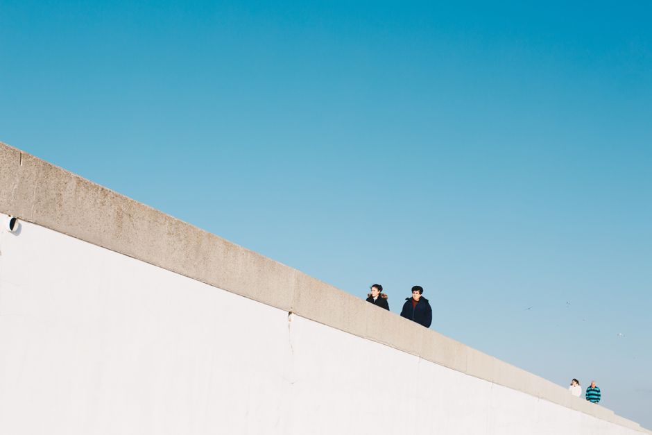 Minimalist photo of people walking along a white wall against a clear blue sky. Perfect for conceptual or modern themes.