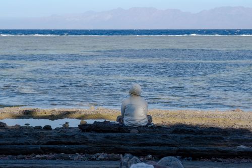 Free Person in white hoodie sitting by the ocean reflecting on the serene landscape. Stock Photo