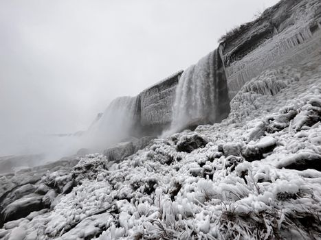 A captivating view of a frozen waterfall surrounded by snow and ice-covered rocks.