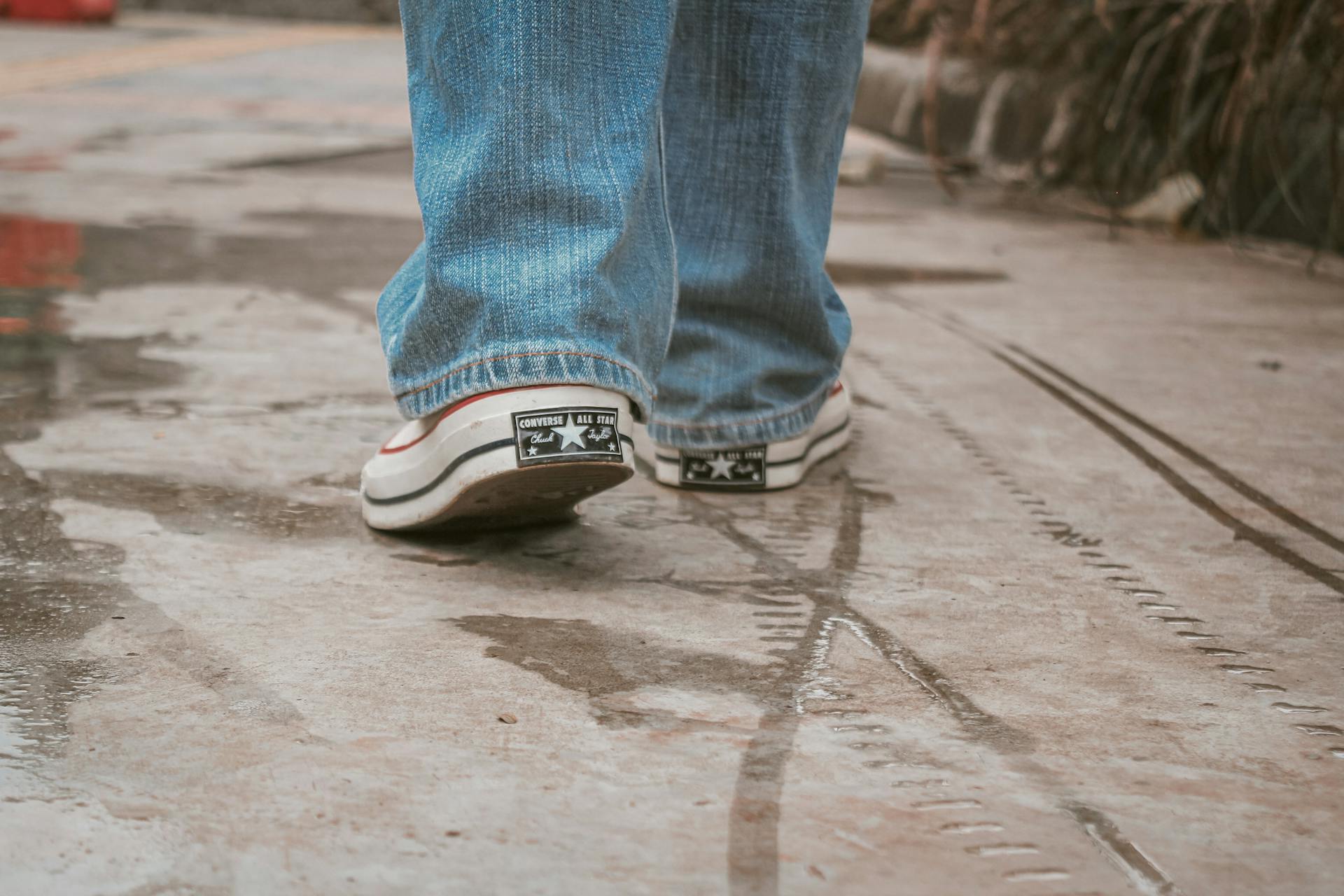 Rear view of Converse sneakers walking on wet pavement. Casual outdoor city scene.