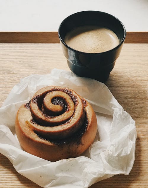 Free A Mouthwatering Bread Beside a Cup of Coffee on a Wooden Surface Stock Photo