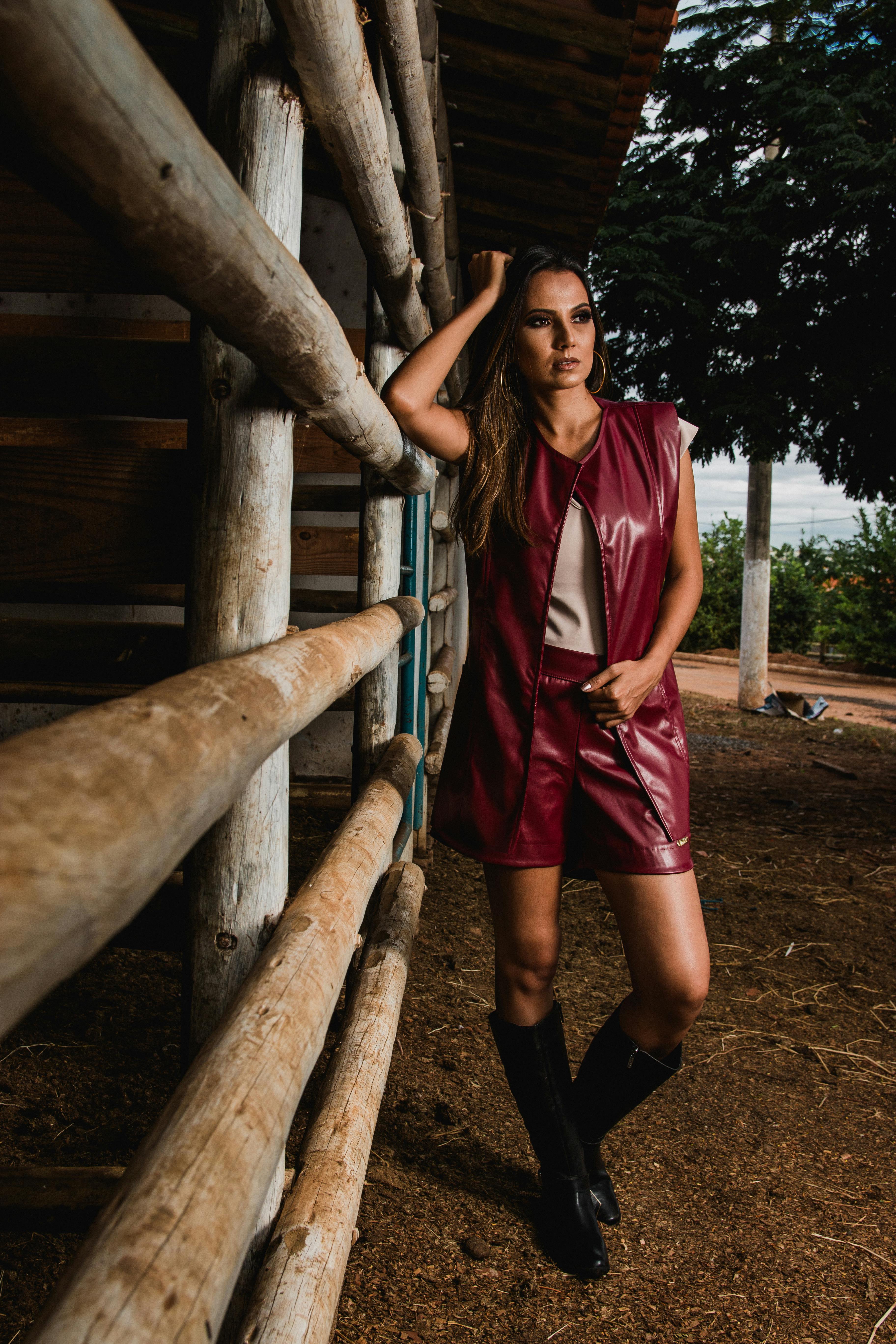 woman wearing maroon leather sleeveless jacket beside horse stable