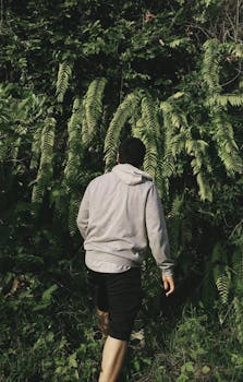 A man in a gray hoodie explores a dense fern forest in Wonosari, Indonesia, creating a sense of adventure.