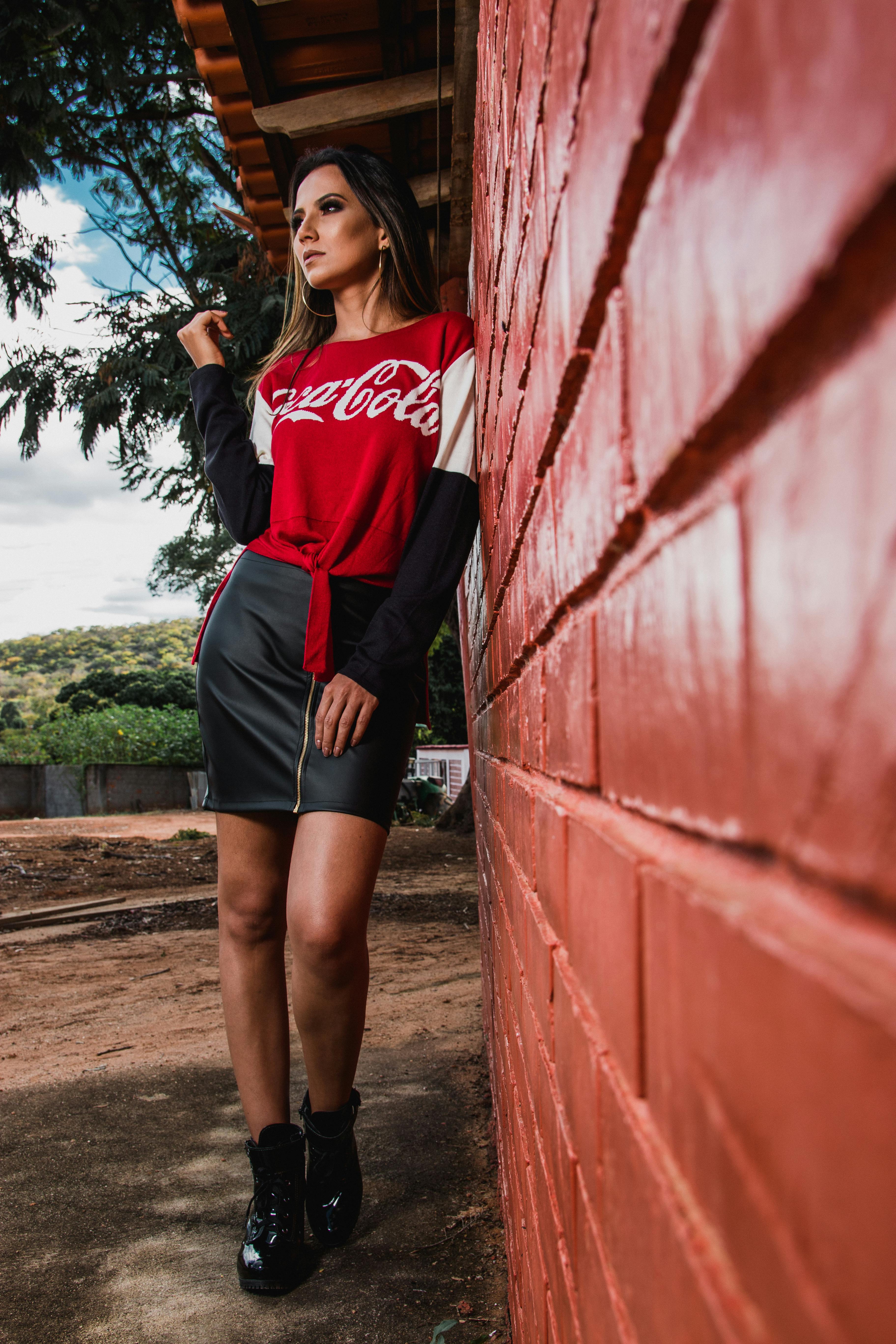 一位穿着红色上衣和黑色裙子的时尚女性在砖墙外摆姿势，散发着风格与自信